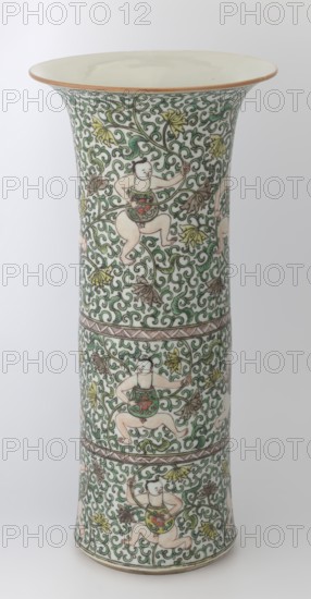 Cylindrical vase of the horn type, Chinese, Qing dynasty Kangxi period, 1662–1722, colored porcelain in the famille verte palette with green family enamels, decorated with lotus tendril ornament and belt decoration, ceramic vessel, height 37.5 cm, diameter 18.0 cm, weight 2.35 kg., A tall flared ceramic vessel with an off-white interior rim and a narrow neck that widens at the top and base, decorated overall with an intricate scrolling vine pattern in green, interspersed with leaves and flowers in yellow and brown. The vessel surface features several repeating figures of a childlike person with pale skin tones and black hair, depicted in dynamic poses and wearing small colored garments with red and green motifs. Thin brown bands encircle the piece separating sections of the pattern, and the background areas remain a pale white. Overall colors visible include white, green, yellow, brown, black, red, and pale skin tones.