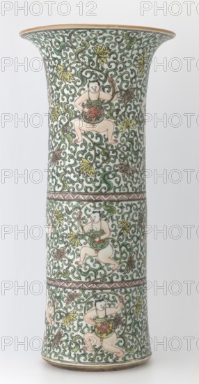 Cylindrical horn type vase, maker, Chinese, Qing dynasty, Kangxi period 1662–1722; colored porcelain in the famille verte green palette; lotus tendril ornament and belt decoration; vessel height 37.5 cm, diameter 18.0 cm, weight 2.35 kg., A tall flared ceramic vase decorated all over with an intricate scrolling vine pattern in green on a white background, featuring a repeating motif of a chubby childlike figure in pale flesh tones engaged with the vines, each figure wearing a green garment with a central round ornament in red and orange and holding parts of the vine; the vine design includes a few yellow and brown stylized leaves and occasional darker green accents, with thin brown band borders separating vertical sections, and a narrow brown rim at the top and base.