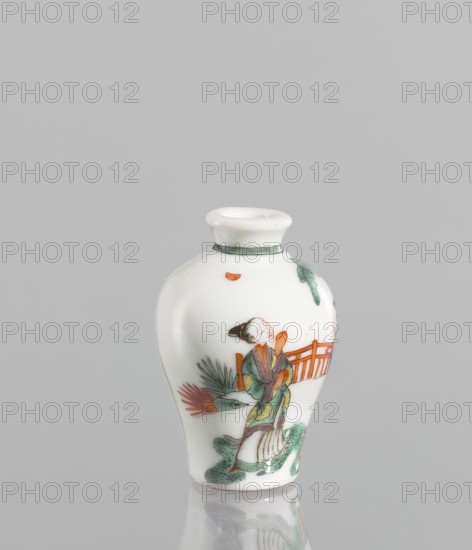 A baluster-shaped snuffbox flask, significantly widened at the shoulders, made of thick white-bodied porcelain white cake. Decorated with a fragment of landscape and architecture and figurative scenes including images of women. Colored porcelain, 18th century, China. Vessel; height 6.9 cm, width 4.6 cm., A small white porcelain vase with a rounded shoulder and narrow neck, decorated with a painted scene showing a person wearing a robe in shades of green and purple with orange accents, standing near a reddish-orange fence and green foliage; additional painted elements include green leaves and a small orange shape near the neck; the vase sits on a reflective surface and the background is a uniform light gray.