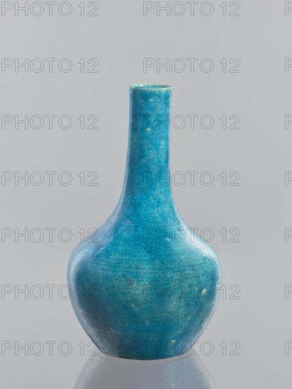Vase-bottle, ; Chinese; Qing dynasty 1644–1911; glazed crackleware ceramics; 19th–20th century; vessel. Height 18.4 cm, diameter 10.8 cm, weight 0.35 kg., A single ceramic vase with a rounded body and a long narrow neck stands centered against a plain light gray background, the vase showing a mottled turquoise blue surface with variations of teal, aqua, and small pale greenish patches and a few tiny darker spots, its surface appearing slightly glossy and textured and reflected faintly on the smooth surface beneath it.