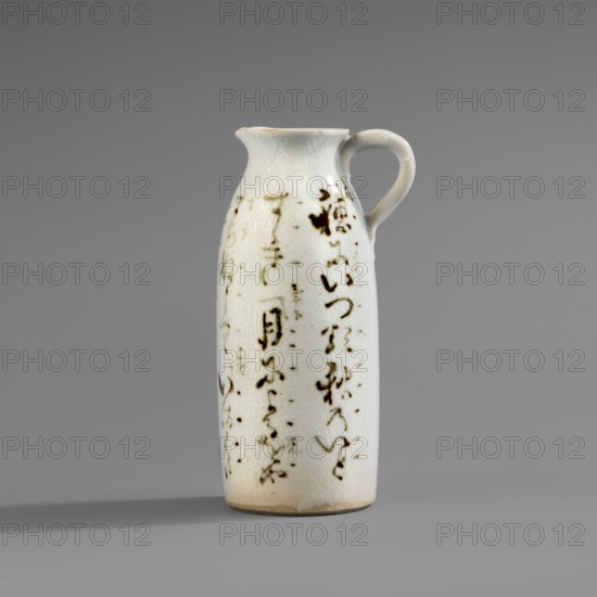 Cylinder-shaped jug with small handle and widened spout. White glaze with fine crackle; decoration painted underglaze with iron oxide black. Inscriptions; Japanese calligraphy. Ceramics, Japanese; 2nd half of the 19th century., Vessel, height 11.7 cm, width 6.3 cm, diameter 4.7 cm., A tall ceramic pitcher with a narrow, rounded body and a small curved handle sits against a plain gray background, the pitcher glazed in a pale off-white with a network of fine crackle lines visible on its surface; scattered across the body are several irregular dark brown brushlike marks and smudges that form vertical patterns, and the rim and base show subtle warm beige discoloration, while the handle matches the off-white glaze and the overall scene includes muted gray tones in the background and shadow.
