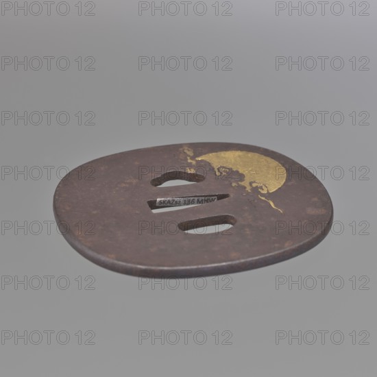 Crossguard tsuba, Senryûsai, Yasumitsu; Ichiryû school; Hanabusa Itchô 1652–1724 — painting design. Tsuba in the shape of a rectangle with rounded corners nadegaku gata with an edge slightly raised above the surface uchi kaeshi. Decorated in low relief with figures of two immortals, Jittoku and Kanzan, reading a scroll; on the reverse a landscape with a golden sun disc emerging from behind clouds. Details and ornament of the characters' costumes executed with gold inlay using the nunome technique. Edo period 1603–1868, Japan Mito. Tsuba sword crossguard, height 8.7 cm, width 8.0 cm, depth 0.4 cm. Notes: Hanabusa Itchô's painting served as a model for the decoration; his work blends Kanô-school tendencies with ukiyo-e influences., A round, flat metal object with a dark brown, rusted surface and a patch of gold-colored decoration near its edge, featuring a few elongated and rounded cutouts in the center; the background is a smooth, uniform light gray.