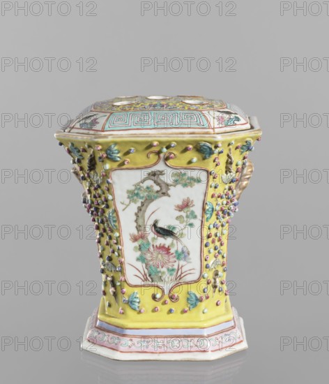 Vase with a lid; ceramics; colored porcelain; openwork perforated flat lid; decorated with flowers, birds, plant ornaments including lotus tendril and meander ornament; Chinese; 19th century, height 27.0 cm, width 15.0 cm., A hexagonal ceramic container with a fitted lid sits against a neutral gray background; the body and lid show a bright yellow background with raised bead-like decorations in pink, blue, purple, and green, and panels framed in white that depict a bird perched among branches and flowers painted in muted greens, pinks, and blues with brown accents; the lid top features geometric banding in turquoise and pink and additional painted floral motifs in yellow, green, pink, and blue; the base shows a band of pale pink and white with a scrolling motif in turquoise and pink; the overall palette includes yellow, white, pink, turquoise, green, blue, purple, brown, and gold-toned highlights.