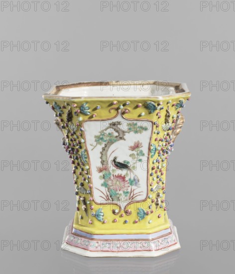 Vase with a lid; ceramics; colored porcelain; openwork; flat perforated lid; Chinese; 19th century ; height 27.0 cm, width 15.0 cm; decorated with flowers, birds, meander ornament, plant ornaments, lotus tendril ornament; vessel., A decorative hexagonal ceramic vessel with a flared rim standing on a matching base, predominantly yellow with areas of white, pink, green, blue, purple, gold, brown, and black. The central white panels on the sides show painted botanical motifs including flowers, leaves, a tree trunk, and a bird with dark and greenish plumage. The yellow background around the panels is covered with raised bead-like dots in pink, purple, blue, and green, and small raised leaf-shaped decorations in green and blue. The vessel has gilded handles on the sides with a twisted rope-like appearance in gold. The base features a pale pink band and a decorative border with scrolling motifs in green and pink on a white ground. The interior rim shows a worn brownish edge and the interior ...