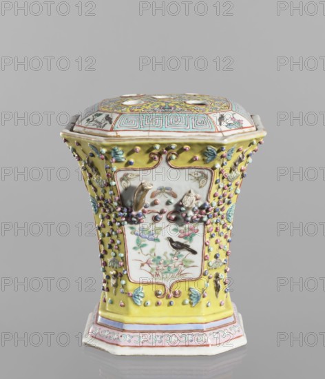 Vase with a lid, ceramics; colored porcelain, openwork; flat perforated lid; decorated with flowers, birds, plant ornaments, lotus tendril ornament, and meander ornament; 19th century, China; height 27.0 cm, width 15.0 cm., A painted ceramic vessel with a hexagonal shape and lid sits against a neutral gray background; the piece features a dominant yellow glaze on its body, with panels of white showing painted floral and bird motifs in colors including green, pink, blue, brown, and black, and small raised bead-like decorations in pastel shades of pink, blue, purple, and green scattered across the yellow areas; the lid displays geometric and floral patterns with turquoise, pink, yellow, and gold tones, and the base has bands of pale pink, blue, and white with a decorative border.