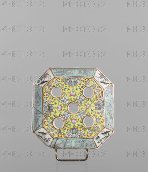 Vase with a lid, ceramics, colored porcelain, openwork perforated lid, decorated with flowers, birds, meander ornament, plant ornaments and lotus tendril motif. Flat, perforated lid. 19th century, China. Vessel. Height 27.0 cm; width 15.0 cm., An octagonal ceramic object with a central panel decorated in bright yellow and detailed with floral and scrolling motifs in pink, green, blue, and white, containing a grid of circular cutouts; the wide border features a repeating geometric pattern in turquoise and white with thin reddish outlines and small triangular corner panels painted with floral designs in pink, green, and black; the piece rests on a small metallic stand that is gold in color, and the background is a smooth neutral gray.