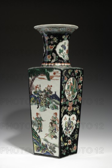 Vase from the famille noire, ; Chinese, Qing dynasty Kangxi, 1662–1722; colored porcelain with painted medallions depicting butterflies, figurative scenes, and plant motifs; vessel vase; height 44.5 cm, width 14.2 cm, depth 14.6 cm., A tall, rectangular ceramic vase with a flared neck sits against a dark background. The vase displays a glossy black background on several faces, densely decorated with floral motifs in green, pink, white, orange, and pale blue, along with a few large white cartouche shapes filled with additional flower designs. Other panels on the vase show a light, creamy background with painted human figures wearing colorful garments in green, orange, blue, and yellow, set within a landscape of stylized trees, rocks, and a bridge rendered in shades of green, blue, and brown. The flared neck is predominantly black with scattered floral patterns and pale decorative bands near the rim, and the rim itself is a pale off-white. The overall palette includes black, white, green...