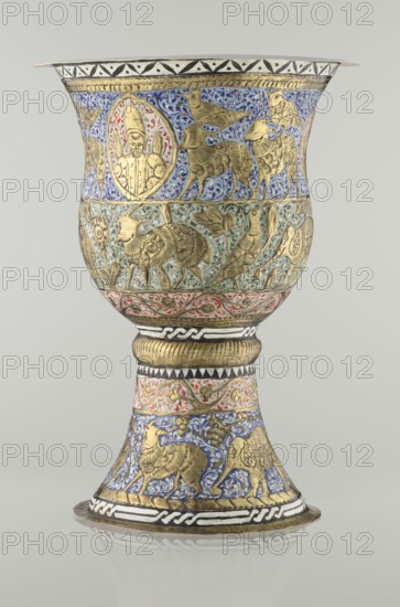 Cup, Persian, Qajar dynasty 1785–1925, 19th century; earthenware vessel, height 25.5 cm, diameter 18.4 cm. Decoration: cartouches with a bust of a man, animals lions, birds, figures, flowers, geometric and small plant ornament; figurative motifs., Iran., A decorative chalice-shaped object stands against a plain light gray background, featuring a flared cup and a tapered stem with a round base. The surface is richly ornamented with embossed golden figures and motifs set against painted backgrounds in blue, green, red, white, and black. The upper band of the cup shows a blue background with scrolling floral patterns and several stylized golden animals and a single framed humanlike figure. Below that is a greenish band with leafy tendrils and more golden animal figures, followed by a narrow red band with vine motifs. The stem includes alternating bands of geometric black-and-white patterns, a ribbed golden collar, a red floral band, and a lower blue band with golden birds and animals. The...