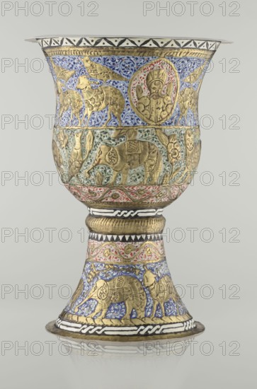 Cup, Persian, Qajar dynasty 1785–1925, 19th century, Iran. Ceramic vessel, height 25.5 cm, diameter 18.4 cm. Decoration: cartouches with a bust of a man, animals lions, birds, figures, flowers, geometric and small plant ornament; figurative motifs., A decorative metal goblet with ornate embossed reliefs and enamel work, showing a wide flared bowl above a narrow waist and a flared foot, predominantly displaying gold-colored metal reliefs set against areas of blue, green, red, white, black, and pale gray enamel; the upper bowl band features gold animal figures and a circular medallion with a human figure outlined in red on a blue floral background, the mid section shows gold elephant and bird motifs on a green leafy background with a red and white patterned border below, the stem area includes a ribbed gold section and bands with black and white geometric designs and red floral scrolls, the foot repeats gold animal reliefs on blue enamel and finishes with a white and black braided band a...