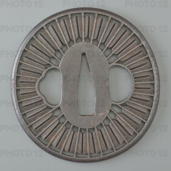 Crossguard tsuba, Tsunetada maker, Japanese, Edo period 19th century. Round tsuba maru-gata with a rounded edge maru-mimi. Decorated with an openwork positive design of thirty-two concentrically arranged arrow shafts and feathers with fine engraved details. Inscribed or associated with Bushu Musashi. Materials and function: sword crossguard for katana; melee weapon accessory. Origin: Kawagoe, Japan. Dimensions: height 7.2 cm; width 7.0 cm; depth 0.3 cm., A round metal object with a central elongated oval opening and two rounded side openings, featuring a raised rim and an intricate radial pattern of narrow, textured slats around the center; the surface shows areas of smooth and rough metal with subtle pitting and wear. The piece displays several shades of gray and brown with hints of muted bronze and darker metallic tones.