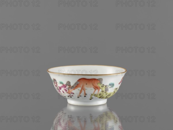 Bowl, ceramics, colored porcelain, Qing style 1644–1911, 19th century, China. Bowl on a ring-shaped foot, height 5 cm, diameter 11.8 cm. Decorated on the outer wall with landscape motifs and horses. Creator, inscription or attribution: Krieg doctor. Repossession/provenance noted Jelenia Góra., A small white porcelain bowl with a thin gold rim sits against a gray background, showing painted decorative imagery around its exterior in colors including orange, yellow, pink, green, brown, and gray; the bowl has a flared shape with a short foot and its painted motifs appear reflected faintly on the glossy surface beneath it.