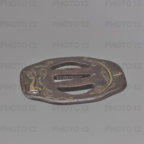 Crossguard tsuba, Jingo Shigenaga ?-1854 and Shimizu fifth master of the Shimizu family makers. Tsuba in the shape of nademokkô otafuku gata; large ryôhitsuana of the same three-petalled shape, developed in the Gotô school and later popularised by the Higo school. Decorated with brass inlay, in high and low relief takazôgan, hirazôgan, depicting a pilgrim's hat and bag on the obverse, and two crossed arrows on the reverse. Signed by the fifth master of the Shimizu family. Edo period, Tenpô era 1830–1844, 1st half of the 19th century. Japan, Yatsushiro. Tsuba. Height 7.8 cm; width 6.5 cm; depth 0.3 cm., A flat, irregularly rounded metal object with a central rectangular opening and two parallel slots, showing a dark brown patina with areas of lighter brown and small highlights of gold; there is a decorative curved inlaid motif on one side in gold and an abstract raised design on the opposite side in gold and darker tones, all set against a plain light gray background.