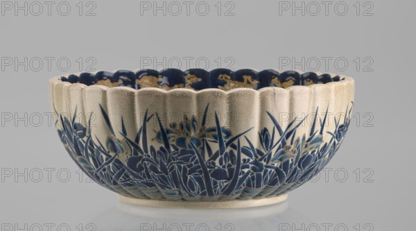 Bowl, Toyota Masanobu craftsman, Satsuma ware, 2nd half of the 19th century Meiji period, Japan, Kagoshima. Deep bowl on a low ring-shaped base with a knobbed body and serrated rim reminiscent of a chrysanthemum. Outer wall: clumps of blooming irises growing from water, flowers and leaves painted in two-tone blue enamel with gold outlines and stylized waves/ripples. Inner surface: large gold chrysanthemum rosette imperial crest in the mirror with the Tokugawa family coat of arms in the center; side wall filled with dense, colorful ornament of various chrysanthemum flowers and butterflies in white, red, blue, gold, and green overglaze enamels and gold. Top near the edge: uniform cobalt blue valance ornament. Signature on the base painted in gold reading: Satsuma yaki, Satsuma kuni, Ijun'in workshop, Toyota Masanobu. Vessel; height 12.0 cm, diameter 28.0 cm., A shallow scalloped ceramic bowl with a crackled cream exterior and a deep blue interior rim is shown, decorated around its outer ...