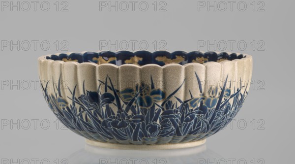 Bowl, Toyota Masanobu workshop, Satsuma ware, 2nd half of the 19th century Meiji period, Japan, Kagoshima. Deep bowl on a low ring-shaped base with a knobbed body and serrated rim, form reminiscent of a chrysanthemum. Outer wall decorated with clumps of blooming irises emerging from water; flowers and leaves painted in two-tone blue enamel, outlines and stylized waves/ripples in gold. Inner surface with a large gold chrysanthemum rosette imperial emblem in the mirror, Tokugawa family coat of arms inscribed in the center; side wall filled with dense, colorful ornament of various chrysanthemum flowers and butterflies in white, red, blue, gold, and green overglaze enamels and gold. Top edge finished with a uniform cobalt-blue valance. Signature on the base in gold reading: Satsuma yaki, Satsuma kuni, Ijun'in, Toyota Masanobu. Vessel height 12.0 cm, diameter 28.0 cm., A shallow scalloped ceramic bowl with a crackled off-white exterior rim and interior edge, decorated around its lower exter...