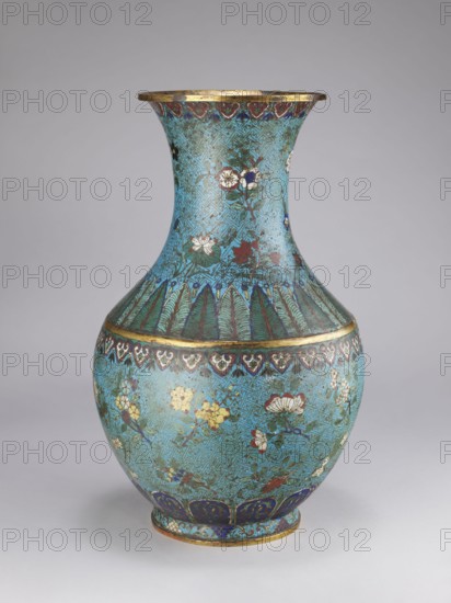 Vase, Chinese, Qing dynasty 1644–1911, 18th/19th century. Porcelain vessel with a thick cylindrical neck and a flared spout, decorated with chrysanthemums, peonies, plum trees, meander ornament and plant motifs. Height 61.5 cm; diameter 25.7 cm; weight 10.0 kg., A single ornate vase with a bulbous body and a flared neck standing on a small rounded foot, decorated overall in a bright turquoise background with an intricate, repeating geometric pattern. The vase features floral motifs in a few colors including white, red, yellow, dark blue, and green, with leaves and stems in various shades of green. Bands of decorative patterns encircle the vase near the neck, shoulder, and foot in colors such as gold, dark blue, and reddish-brown. The rim and some accent lines appear metallic gold. The base area shows a darker blue paneled design, and the neck area has a series of vertical leaf-like motifs in green and dark blue. The surface shows slight variations in tone and some areas with darker mot...