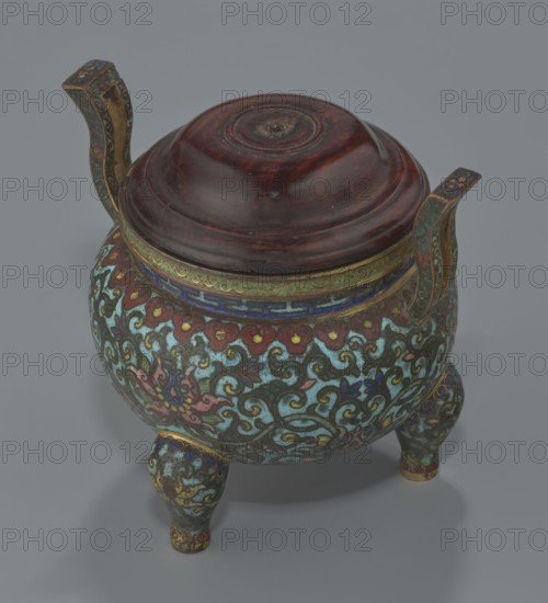 Ding-type incense burner with cover, Chinese, Qing dynasty, Qianlong period 1736–1795. Ceremonial ding vessel/censer decorated with plant ornament lotuses. Incense burner, vessel; height 11.5 cm, diameter 11.0 cm., A rounded three-legged vessel with a domed wooden lid sits on a gray surface; the body and legs are covered in swirling floral and cloudlike patterns in turquoise, teal, green, red, pink, blue, purple, yellow, and gold, with gilded accents and ornate curved handles rising from opposite sides that feature green, gold, and blue tones, while the lid is a polished deep reddish-brown wood with circular carved rings and a darker central worn spot.
