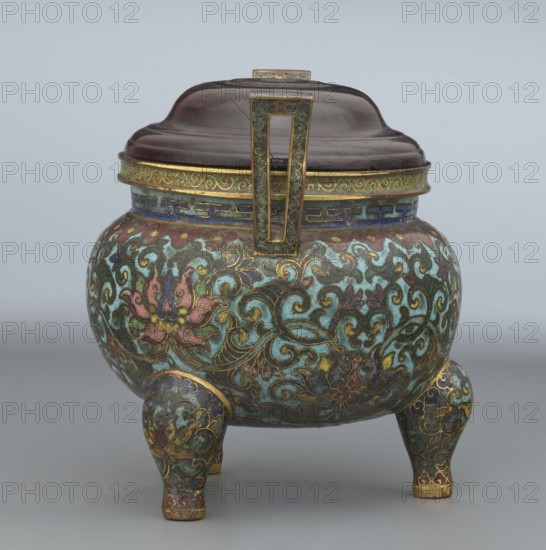 Ding-type incense burner with cover; Chinese; Qing dynasty, Qianlong period 1736–1795; ding vessel/censer for ceremonial use; decorated with plant/lotus ornament; height 11.5 cm, diameter 11.0 cm.,  noted., The image shows a rounded three-legged vessel with a domed lid and a rectangular handle on top, decorated with intricate swirling floral patterns. The main body and legs display a mix of turquoise, teal, green, blue, pink, purple, and gold tones, with gold outlining on the ornate motifs. The lid appears dark brown with subtle reddish highlights and the rim and handle feature gold and blue decorative bands. The overall surface shows a patinated, enamel-like finish with richly colored, detailed ornamentation.