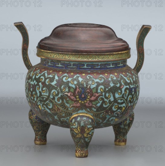 Ding-type incense burner with cover, Chinese, Qing dynasty, Qianlong period 1736–1795. Ceremonial ding vessel/censer decorated with lotus plant ornament. Incense burner vessel. Height 11.5 cm; diameter 11.0 cm., An ornate tripod vessel with a domed lid and two upward-curving handles sits on a neutral gray surface; the body, lid rim, handles, and legs are covered in intricate scrolling floral and foliate patterns in teal, turquoise, green, blue, pink, red, brown, gold, and yellow, with areas of dark brown on the lid and accents of metallic gold along edges and decorative bands, and the vessel rests on three short, decorated legs.