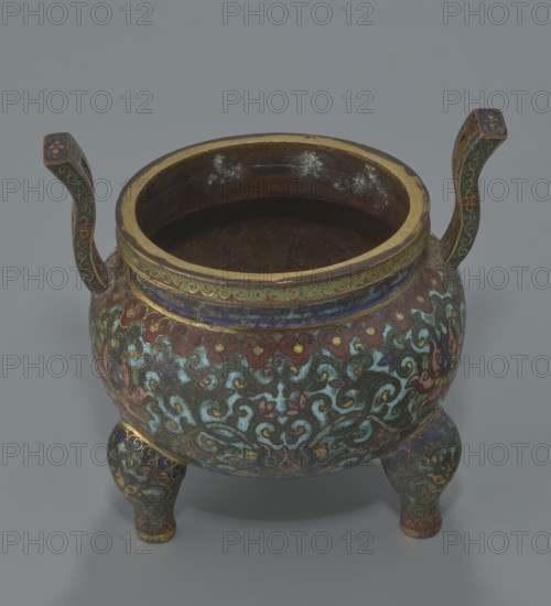 Ding-type incense burner with cover, Chinese, Qing dynasty, Qianlong period 1736–1795. Ceremonial ding-style censer/incense burner decorated with lotus plant ornament. Height 11.5 cm; diameter 11.0 cm., A rounded metal vessel with two upward-curving handles and three short bulbous legs sits against a plain gray background; the vessel displays an intricate swirling floral design in turquoise, green, red, blue, pink, gold, and dark brown, with a wide gold-rimmed opening showing a dark interior and signs of wear, and decorative bands of blue and gold encircling the neck and handles.