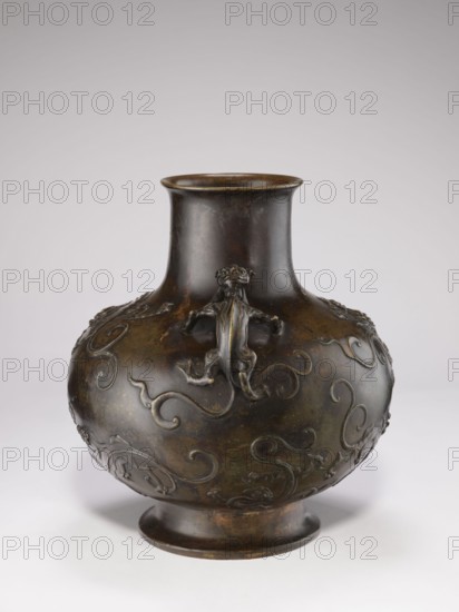 Vase with two dragon-shaped handles qiulong, Chinese, Qing dynasty 1644–1911, 19th century. Porcelain vessel with backdated signatures; belly shaped as a flattened sphere; low, round foot; cylindrical short neck with a very slightly flared spout; dragons iconography. Height 38 cm, diameter 15 cm, weight 10.0 kg., A rounded bronze vessel with a narrow neck and flared rim sits on a low circular foot, its surface showing a dark brown patina with areas of greenish and lighter brown tones; embossed decorative motifs in the form of flowing scrolls and stylized creatures wrap around the bulbous body, and a small sculpted animal figure is attached near the shoulder, all set against a plain pale background.