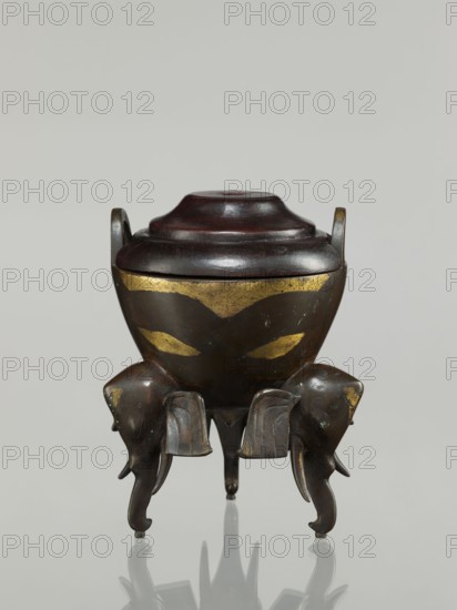 Censer with cover;, Bronze censer with two arched handles and convex cover with two offsets; decorated with elephants. Chinese, Qing dynasty 1644–1911, 19th century. Height 21.1 cm; diameter 14.3 cm., A small lidded vessel with a rounded body and a stepped lid sits on a reflective surface, supported by a group of elephant-shaped legs facing outward; the vessel and lid are primarily dark brown to black with visible reddish-brown highlights on the lid, and there are worn gold-colored decorative patches on the body and on parts of the elephant legs; the elephants show sculpted trunks and ears and the overall scene includes reflections of the object on a pale gray background.