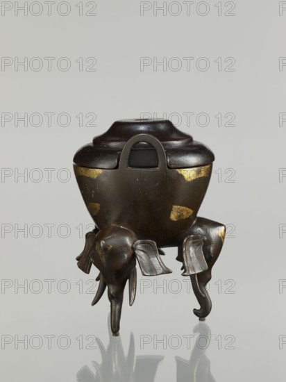 Censer with cover, gift, Chinese art, Chinese, Qing 1644–1911, elephants, ceremonial vessel. Censer with two arched handles; convex cover with two offsets. 19th century, China. Censer; height 21.1 cm, diameter 14.3 cm., A bronze vessel with a dark brown lid sits on three sculpted elephant legs; the vessel body is a dark metallic brown with worn gold patches, and the lid is a slightly richer dark brown with a rounded, stepped profile and a loop handle. The elephant legs are dark bronze with subtle lighter highlights, showing stylized ears and trunks that extend downwards, and the whole object casts a soft reflection on a pale gray surface against a light gray background.