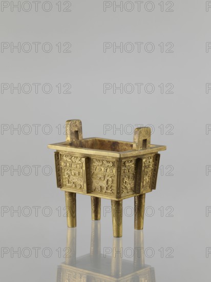 Fangding incense burner with cover, Chinese, Qing dynasty 1644–1911, 19th century. Bronze vessel decorated with archaic ornament in flat relief, featuring taotie and fantastic creatures. Height 15.2 cm, width 14.0 cm, depth 10.9 cm., Ceremonial vessel., A small rectangular metal vessel with a golden color sits on a reflective surface, supported by four cylindrical legs that taper slightly and show engraved decorative patterns; the vessel has a flat rim with two raised tab-like handles at opposite ends and detailed low-relief ornamental designs on each vertical panel of its sides, all in matching golden tones with subtle darker patina in recessed areas, and the background is a smooth neutral gray.