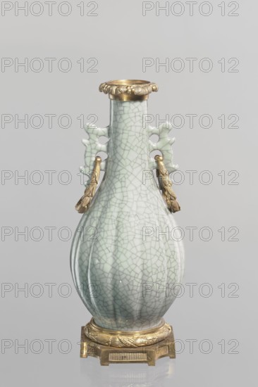 Vase, Chinese, Qing 1644–1911, 19th century. Celadon ceramic slender vase with a long neck and bottle-shaped belly; set on a metal base. The spout is framed with a metal ring decorated with acanthus leaves. Height 23.3 cm; diameter 11.5 cm; weight 1.5 kg., A pale celadon glazed vase with a crackled surface stands on a decorative gilt base; the vase has a rounded pear-shaped body tapering to a narrow neck and rim, with two ornamental openwork handles on the sides from which hang gilt sculpted pendants; the glaze shows a network of thin crackle lines in shades of pale green and off-white, and the metal fittings and base are a warm gold color, all set against a neutral light gray background.