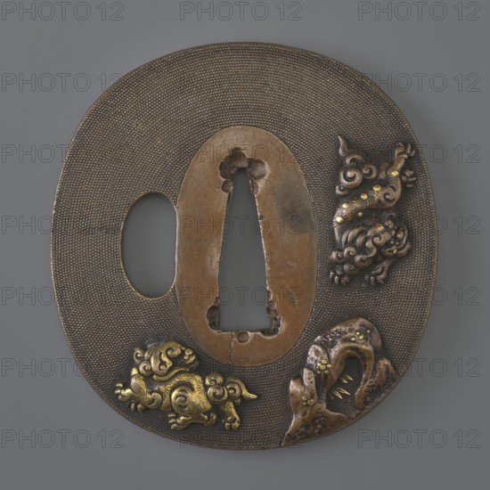 Crossguard tsuba by Kikuoka Masayoshi; oval tsuba tatemaru gata with rectangular edge kaku mimi, katahitsu ana, oval seppa dai. Decorated in high relief using the iro-e takazôgan technique inlaying with multicolored metals on a grained nanako background. Obverse shows two karashishi Chinese guardian lions by a rock; reverse depicts a waterfall flowing among rocks. Signature on the reverse. Japan, 1st half of the 19th century Edo period, 1603–1868. Materials/function: tsuba sword crossguard for katana. Dimensions: height 6.8 cm, width 6.3 cm, depth 0.3 cm., A rounded metal object with a textured brown surface and a central smooth brown area featuring an elongated cutout, decorated with a few ornate raised embellishments in metallic gold and darker bronze tones; one embellishment shows swirling cloud-like forms, another resembles a curled creature with gold highlights, and a third is a rock-like form with embedded gold accents, all set against a muted gray background.