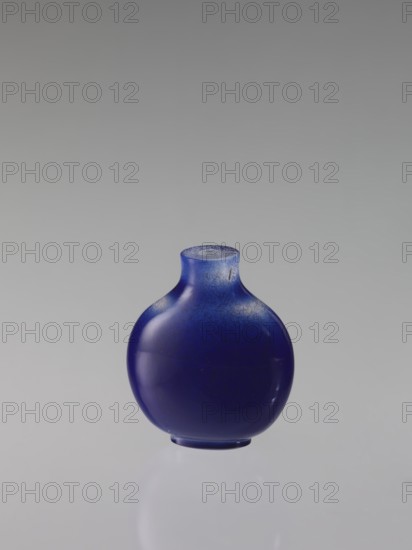 Flask snuffbox, maker, 18th century Qing dynasty, China. Round, flattened-belly vessel; height 6.8 cm, width 5.6 cm. Chinese art; snuff flask., A small round bottle with a short neck and flattened base sits centered against a smooth gray background; the bottle is a deep cobalt blue with lighter blue speckling and subtle highlights, and its surface shows glossy reflections and a slightly frosted rim.