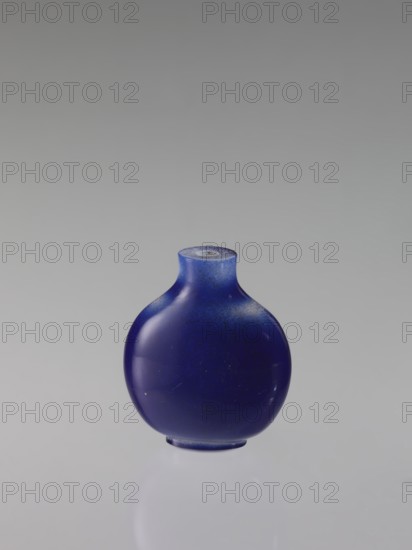 Flask snuffbox, creator, 18th century, Qing dynasty 1644–1911, China. Round, flattened-belly vessel; height 6.8 cm, width 5.6 cm. Chinese art., A small rounded bottle with a short neck and flattened base sits centered against a smooth neutral background; the bottle is deep blue with areas of lighter blue speckling and subtle glossy reflections, and its surface shows a few tiny spots and faint scuffs.