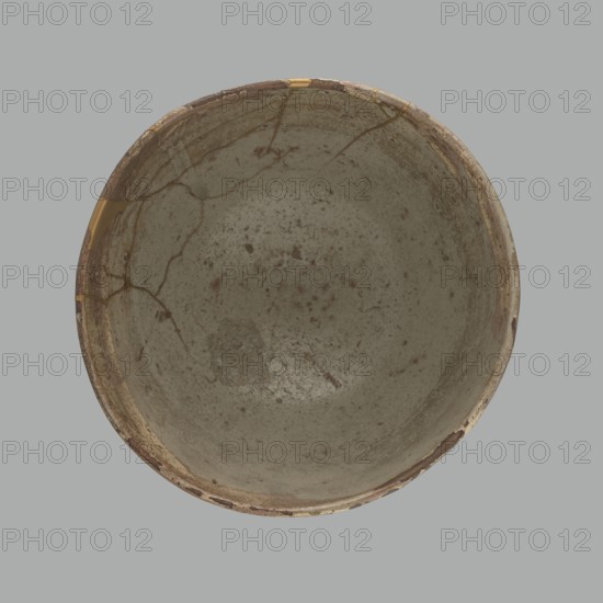 Wan-nari type tea bowl wan-nari chawan, maker, Japanese, Edo period 18th–19th century. Stoneware bowl on a low, round foot; rough surface; partly glazed with white milky and grey-bluish glazes with numerous spots and drips, gold-lacquer veins. Fillings and gluing made with gold lacquer. Function: tea vessel chawan. Height 8.4 cm; diameter 13.5 cm., A top-down view of a round bowl with a weathered, speckled interior surface showing a few cracks and repaired seams; the bowl displays tones of gray, beige, brown, and a few touches of gold along some of the repaired lines, set against a solid light gray background.