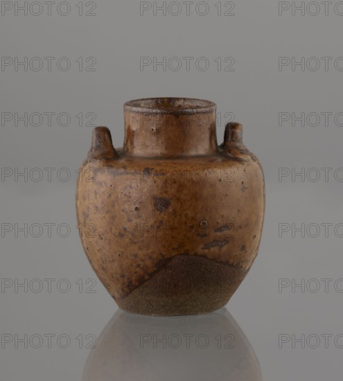 Tea canister chaire of the mimitsuki type, Japanese, Edo 1603–1868–Meiji 1868–1912, 19th century. Brown container with two handles and a lid in a navy blue brocade silk bag. Dark brown porous wheel-thrown clay with light brown glaze showing rough air-bubble cracks; plastic handles. Owari, Japan. Vessel; height 6.3 cm, diameter 5 cm. Tea, chaire vessel, ceramics., A small rounded vessel with a short cylindrical neck and two small stubby handles near the top sits against a plain grey background and is reflected on a glossy surface below; the vessel has a mottled brown surface with darker brown speckles and patches, a rougher darker brown area at the base, and variations of tan and ochre tones across its body.
