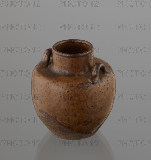 Tea canister chaire of the mimitsuki type, Seto; gift; Japanese, Edo 1603–1868–Meiji 1868–1912; ceramics; container chaire for tea. Brown container with two handles and a lid in a navy blue brocade bag silk. Dark brown, porous wheel-thrown clay; light brown glaze with rough air bubble cracks; applied plastic handles. 19th century; Japan, Owari. Vessel: height 6.3 cm; diameter 5 cm., A small rounded ceramic vessel with a short neck and a narrow open mouth, showing a textured surface with a few small handles near the neck; the vessel displays shades of brown and tan with darker brown speckles and patches and a slightly rougher, darker base, set against a smooth gray background.