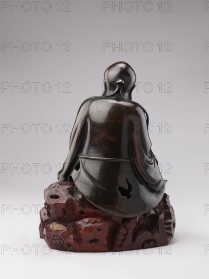 Sage sitting on a rock base;, gift; Chinese art; Chinese; Qing 1644–1911; figurine of a man; Chinese Buddhism; scholar/old man; 18th–19th century; China; sculpture; height 32.5 cm, A dark brown, glossy carved figure seen from behind, seated on a carved reddish-brown base that resembles a group of rocks; the figure wears a draped garment with smooth flowing folds and has a rounded head with a small protrusion at the nape, and the scene includes tones of black, deep brown, reddish-brown, and hints of lighter brown against a pale gray background.