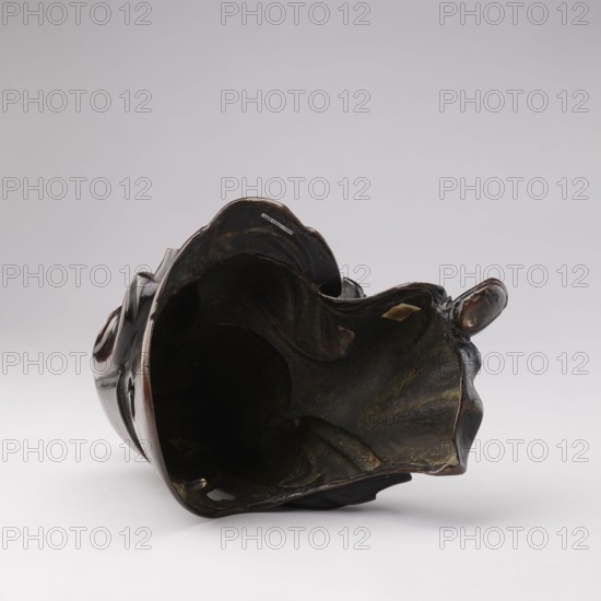 Sage sitting on a rock base, unknown sculptor, Chinese, Qing 1644–1911, 18th–19th century, figurine of a man scholar/old man related to Chinese Buddhism, sculpture, height 32.5 cm., A dark, hollow object lying on its side with an irregular, rounded opening and wavy edges, showing smooth shiny surfaces and rougher inner textures; the object displays colors including dark brown, black, deep greenish tones, a few patches of lighter brown or tan, and small areas of muted yellow; it rests on a light gray surface against a pale gray background, and the shape suggests curving, folded forms with highlights and subtle reflections on the outer surface.