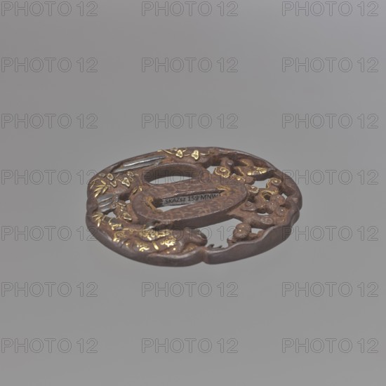 Crossguard tsuba, Sôten, / school, Kitagawa, Sôten, / personal slogans / author, pines, katana, Uba, sword crossguards, Japanese art, Japanese culture, bamboos, plants, waterfalls, swords, weapons, edged weapons, Edo 1603-1868, Tsuba oval tatemaru gata, with an irregular, rounded edge, decorated with a positive openwork pattern, inlaid with gold and shakudô, depicting Uba under a pine tree, by a stream, looking at the sky, in which the moon emerges from behind the clouds. Signed. 1701–1730 Edo Period, 1603–1868, Japan, Ômi Eshu. Tsuba; height 7.1 cm, width 6.7 cm., A round, hollow-centered metal object with an openwork design resting against a neutral gray background, showing a textured brown surface with areas of metallic gold inlay and small accents of darker gray, featuring carved organic shapes and decorative motifs around the central opening.
