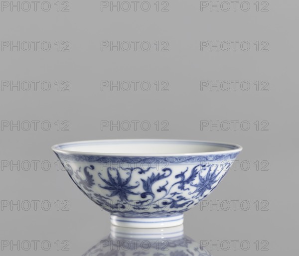Bowl, blue and white porcelain, Chinese, Qianlong style Qing dynasty, 1736–1795. Porcelain vessel decorated with lotuses and lotus tendril ornament. Slightly flared bowl, height 4.3 cm, diameter 9.8 cm., A porcelain bowl with blue floral and scrolling vine patterns on a white background, sitting on a short foot and reflected on a glossy surface; colors visible include blue, white, and shades of gray in the background and reflection.