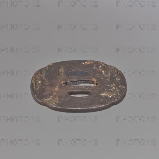 Crossguard tsuba, Jakushi,  school, Jakushi, Kizaemon, / personal slogans / author; katana sword crossguard tsuba in the shape of a mokkô quatrefoil, with a kôgai hitsu hole plugged with shakudo, copper sekigane, textured surface ishime ji. Decoration in low relief hirabori, with fine details inlaid with gold, in places using the nunome technique, and copper. Both sides bear a Chinese-style mountainous landscape with human and architectural staffage — mountains, bamboos, pine trees, bridges. Signed. 18th century Edo period, 1603–1868. Japan; Nagasaki, Hizen. Dimensions: height 7.6 cm, width 6.0 cm, depth 0.4 cm., A round, flat metal object with an uneven, worn surface and irregular edges sits against a plain gray background; the metal shows dark brown and black tones with areas of dull golden highlights and patches of lighter brown; there are a few cutouts and slots in the center and a small raised, smooth oval shape near the top, and the surface texture appears rough with scratches, d...