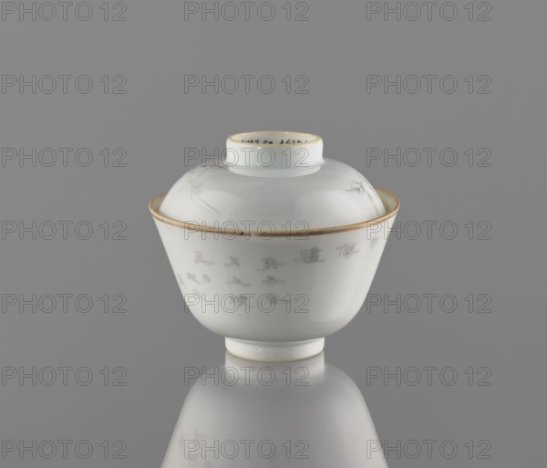 Bowl with a lid, ceramics, colored porcelain; decorated with ducks among reeds drawn in delicate black line and an inscription; lid topped with a branch bearing peach fruit. Qing dynasty, Tongzhi period 1862–1874. Bowl on a ring foot with a lid-stand. China; height 9 cm, diameter 10.3 cm., A white glazed porcelain covered bowl with a round foot and a domed lid sits centered against a neutral gray background; the bowl and lid have a thin gold rim and faint engraved linear designs visible on the lid and body, and the smooth glossy surface produces soft reflections on the gray surface beneath; visible colors include white, gray, and gold.