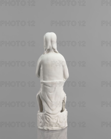 Adam figurine, Chinese, Chinese art, Adam Bible, male figurine, figure of a half-naked Adam, 17th/18th century, China, sculpture, height 20.3 cm, width 7.0 cm, A small white ceramic figurine viewed from behind, showing the back of a seated figure with long hair and draped clothing, sitting on a decorated round base; the scene is set against a smooth gray background with reflections of the base on the surface below.