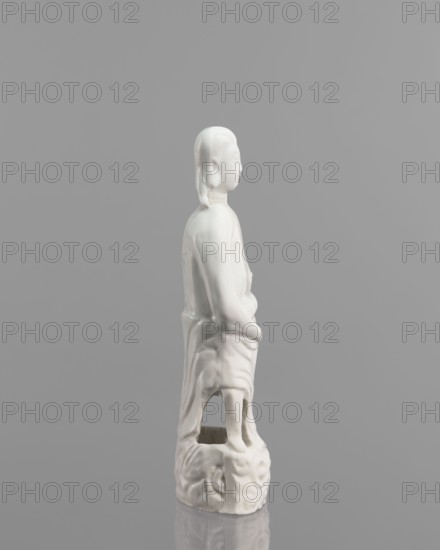 Adam figurine, Chinese, 17th/18th century, sculpture; male half-naked Adam Bible, height 20.3 cm, width 7.0 cm., A white ceramic figure of a person shown in profile standing on a rounded decorative base against a neutral gray background; the figure has smooth features, long hair pulled back, a draped garment with visible folds, hands resting near the waist, and the base has carved swirling patterns with an open area beneath the skirt; colors visible are white for the figure and base and various shades of gray in the background and reflections.