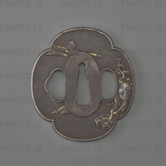 Crossguard tsuba, sword crossguard with landscape motifs depicting fishermen, bridges, rocks, and plants. Plastic decoration: obverse – fisherman sitting by the water against a landscape background; reverse – landscape. 19th century, Japan European copy. Tsuba; height 6.9 cm, width 6.3 cm, depth 0.4 cm., A dark metal ornamental object with a rounded quatrefoil outline featuring a central elongated hole flanked by two irregular oval cutouts, showing a slightly raised border and a textured surface with worn areas; decorative elements include a stylized flowing form on one side and a few scattered metallic inlays in a bright yellow-gold color, while the main metal appears dark gray to brown with subtle lighter gray highlights against a smooth gray background.