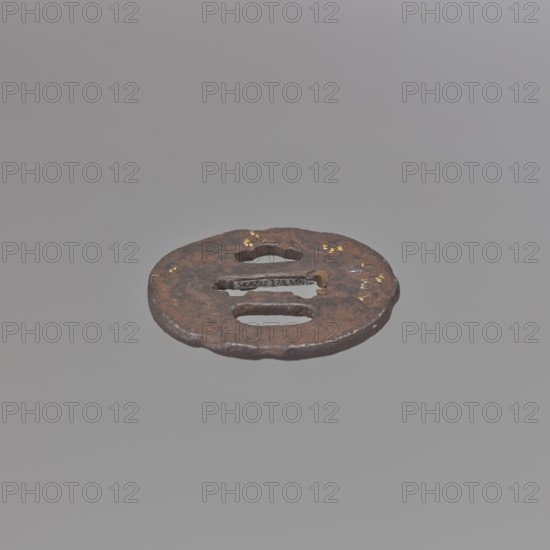 Crossguard tsuba, Kaneie,  school craftsman author. Oval tsuba for a short tantô sword, with an irregularly outlined, wavy uchi kaeshi-type edge and a textured surface, decorated on both sides with a landscape motif. On the obverse: a fisherman on the shore, piled rocks and a hut under a pine tree; on the reverse: a sketchy landscape motif. Details vegetation accentuated with gold inlay, fisherman's head inlaid with shakudô. Signed. 18th century Edo period, 1603–1868, Japan; Fushimi, Yamashiro. Materials/function: tsuba sword crossguard. Dimensions: height 5.7 cm, width 5.2 cm, depth 0.35 cm., A round, flat metal object with a weathered, rusty brown surface floats against a uniform gray background; the object has a few irregular cutouts and a few small spots of gold-colored flecks on its surface, with uneven, slightly rough edges and variations of darker and lighter brown tones.