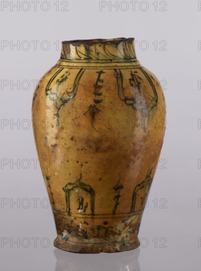 Vase, repossession Glogów, Islamic art, Persian culture, glazed ceramics, utility vase with lambrequin pattern, 18th century, Iran, vessel, height 31.5 cm, diameter 19.7 cm, A ceramic vase with a rounded body tapering toward a narrower base and neck, shown against a pale gray background. The vase surface is glazed in a dominant yellow ochre with areas of darker brown spots and patina. There are decorative painted motifs in dark green distributed around the upper and lower sections, including curved leaflike forms and arching lines, and traces of darker glazing near the rim and base. The rim edge shows a darker brown tone and some irregularities, and the base has a mix of greenish glaze and brown wear. Reflections and glossy highlights appear on the glazed surface.