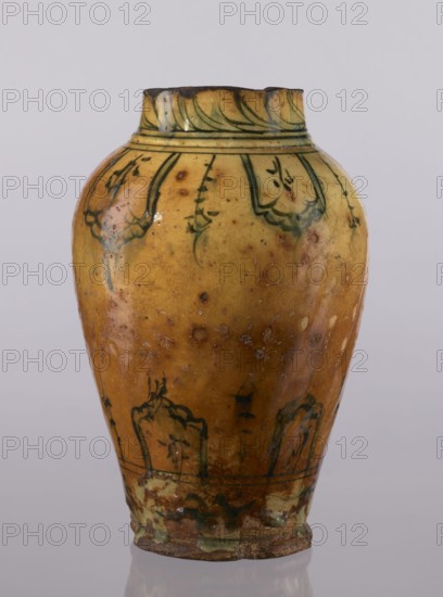 Vase, repossession Glogów, Islamic art, Persian culture, glazed ceramic utility vase with lambrequin pattern, 18th century, Iran; vessel, height 31.5 cm, diameter 19.7 cm, A pottery vase with an oval body narrowing toward a small neck and rim, showing a mottled yellow surface with areas of brown and greenish discoloration, decorated with dark green painted curving floral or leaf motifs around the shoulder and lower body, a darker brown rim edge with some chipping, a glazed sheen with small pitted spots and worn areas, and a darker brownish-green base with irregular glazing and signs of age.