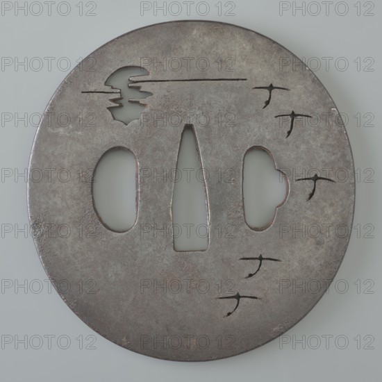 Crossguard tsuba, Tetsugendô, / school, Japanese, Edo period 1603–1868, 18th century. Iron tsuba, round maru gata, flat with a polished surface migaki ji. Decorated with delicate negative openwork forming a motif of a moon partially hidden behind clouds and a flight of wild geese; unsigned. Function: sword crossguard for katana. Dimensions: height 7.1 cm, width 6.9 cm, depth 0.35 cm., A round metal object with a weathered, mottled surface showing shades of gray, brown, and hints of rusty orange, featuring a central elongated triangular opening flanked by two irregular oval openings and a cloud-shaped opening, plus a few small bird-shaped cutouts and linear scratches near the top, all set against a pale gray background.