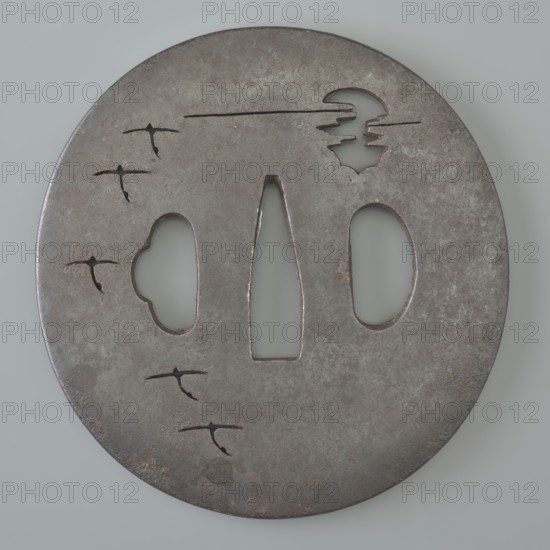 Crossguard tsuba, Tetsugendô,  school author, Japanese art, Japanese culture, Edo 1603–1868, weapons, cold weapons, swords, katana, sword crossguards, tsubas, moons, birds, geese, Tsuba round maru gata, flat, with a polished surface migaki ji. Decorated with a delicate negative openwork creating a motif of a moon partially hidden behind clouds and a flight of wild geese. Unsigned. 18th century Edo period 1603–1868, Japan, tsuba, height 7.1 cm, width 6.9 cm, depth 0.35 cm, A round metal object with a weathered gray and brown surface showing a patina and some darker spots, featuring several cutout shapes including a central vertical elongated cutout flanked by an oval and a cloudlike form, a crescent-like cutout near the top with stepped interior edges, and a group of several small bird-shaped cutouts scattered on the left side; the background behind the cutouts appears a pale gray-green.