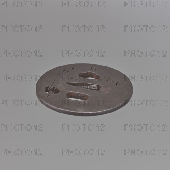 Crossguard tsuba, Tetsugendô,  school author, Japanese art, Japanese culture, Edo 1603–1868, weapons, cold weapons, swords, katana, sword crossguards, tsubas, moons, birds, geese. Tsuba round maru gata, flat, with a polished surface migaki ji. Decorated with a delicate negative openwork creating a motif of a moon partially hidden behind clouds and a flight of wild geese. Unsigned. 18th century Edo period, 1603–1868, Japan. Tsuba; height 7.1 cm, width 6.9 cm, depth 0.35 cm., A round metal disk with a dark brown to black patina floating against a pale gray background, featuring a few irregular cutouts including a rounded triangular hole and elongated oval openings, small engraved marks and short lines on its surface, and areas of lighter brown rust and slight wear around the edges and cutouts.