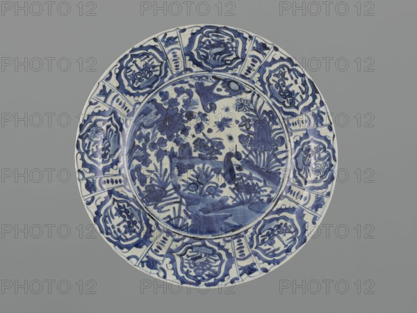 Platter, Safavid dynasty 1501–1736, Persian; ceramics, round deep platter with separate rim on a ring foot. Decoration: in the mirror a pond scene with rocks, three ducks and various aquatic plants and insects; on the collar in eight multi-leafed cartouches cranes and stylized plants; stylized plants on the outer side of the rim. On the reverse a handwritten inscription in Arabic script; within the ring of the foot the words jami'-je Bali handwritten in brown dye, likely referring to an unspecified locality. The asymmetric composition—central rock and a bank jutting into the water with a duck—maintains a circular form without horizontal landscape division. Decoration imitates motifs of blue-and-white Chinese kraak porcelain and alludes to Chinese painting, but Persian ceramic depictions are freer and denser in motifs; plant-animal compositions birds, insects, quadrupeds echo Persian textile and miniature traditions. Nature was a frequent Safavid subject; the first landscape composition...